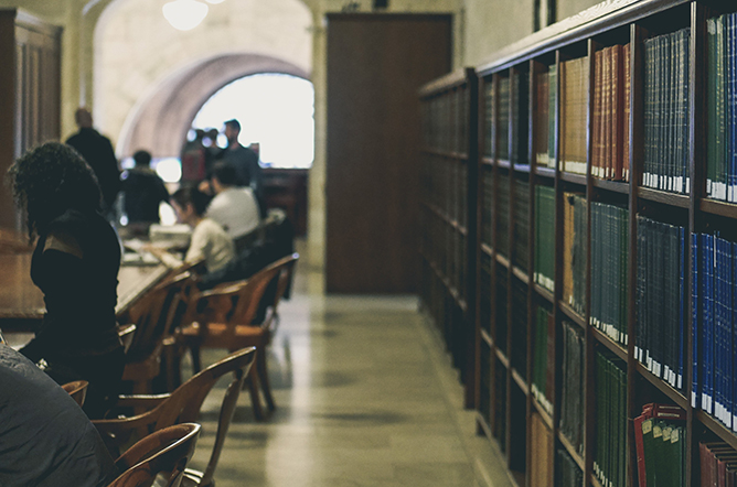 Shelf and tables at a library with a few people sitting and wandering
