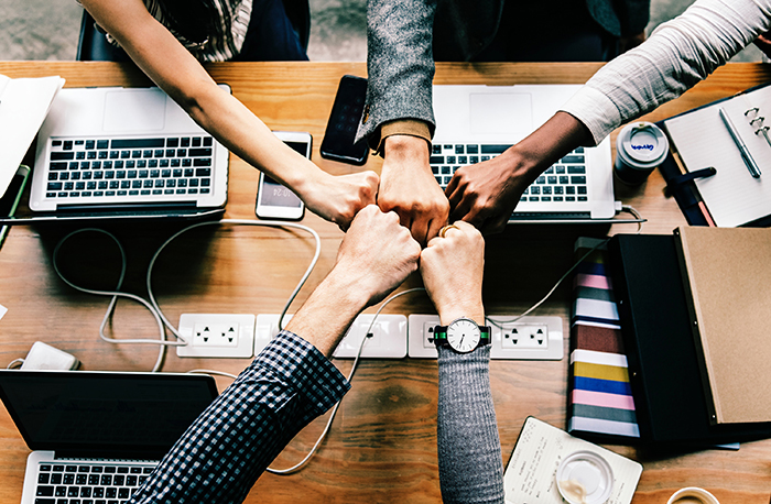 people's hands reaching toward center of computer desk