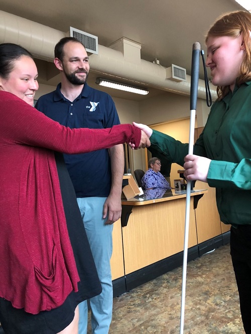 Woman with a white cane shakes another woman’s hand.