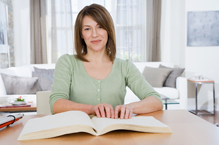 Seated woman reads a Braille book.