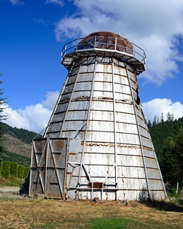 Rusted wigwam burner rises toward deep blue sky splotched with cotton colored clouds