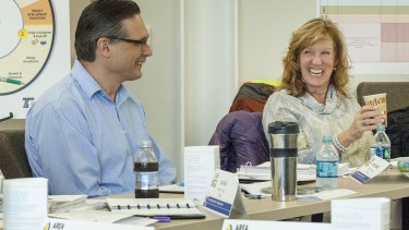 Two employees sitting and laughing together. One of them is holding a cup.