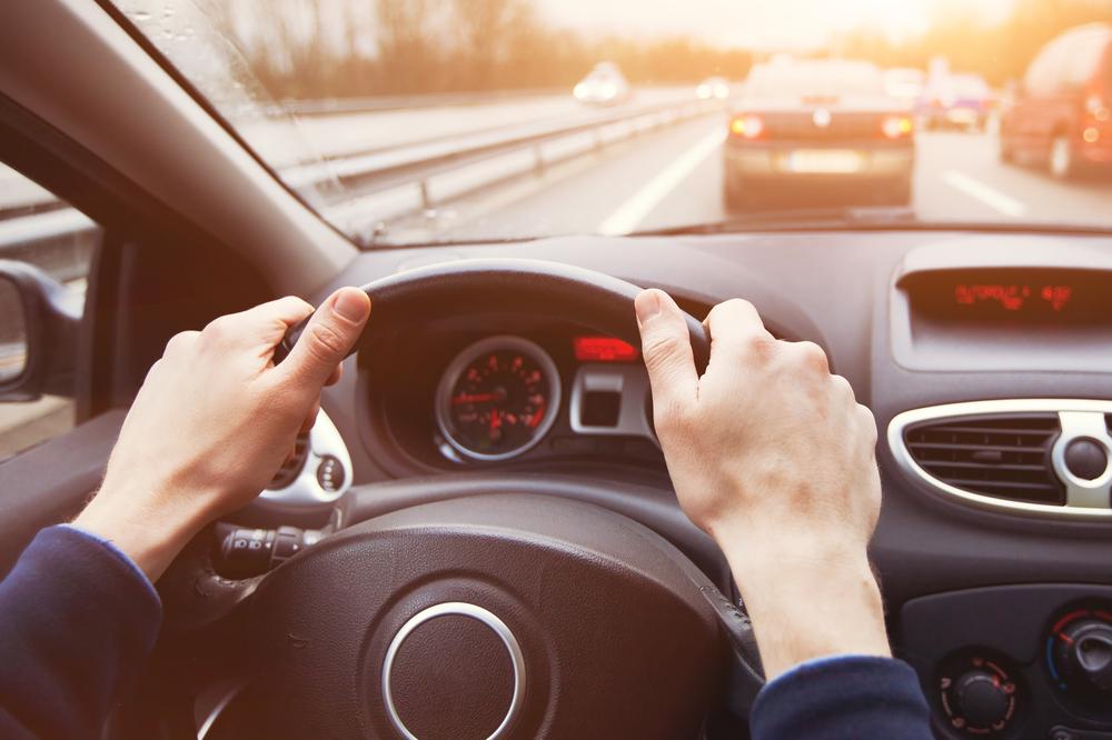 Un conductor sujeta el volante con las dos manos. Hay otro auto adelante.