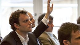 Group of people at a meeting; one person with a hand raised
