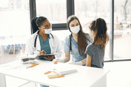 A child stands before two smiling health care providers at a desk