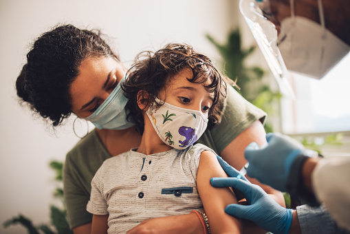 Masked Parent Holding Masked Child Receiving Shot From Masked Health Care Provider