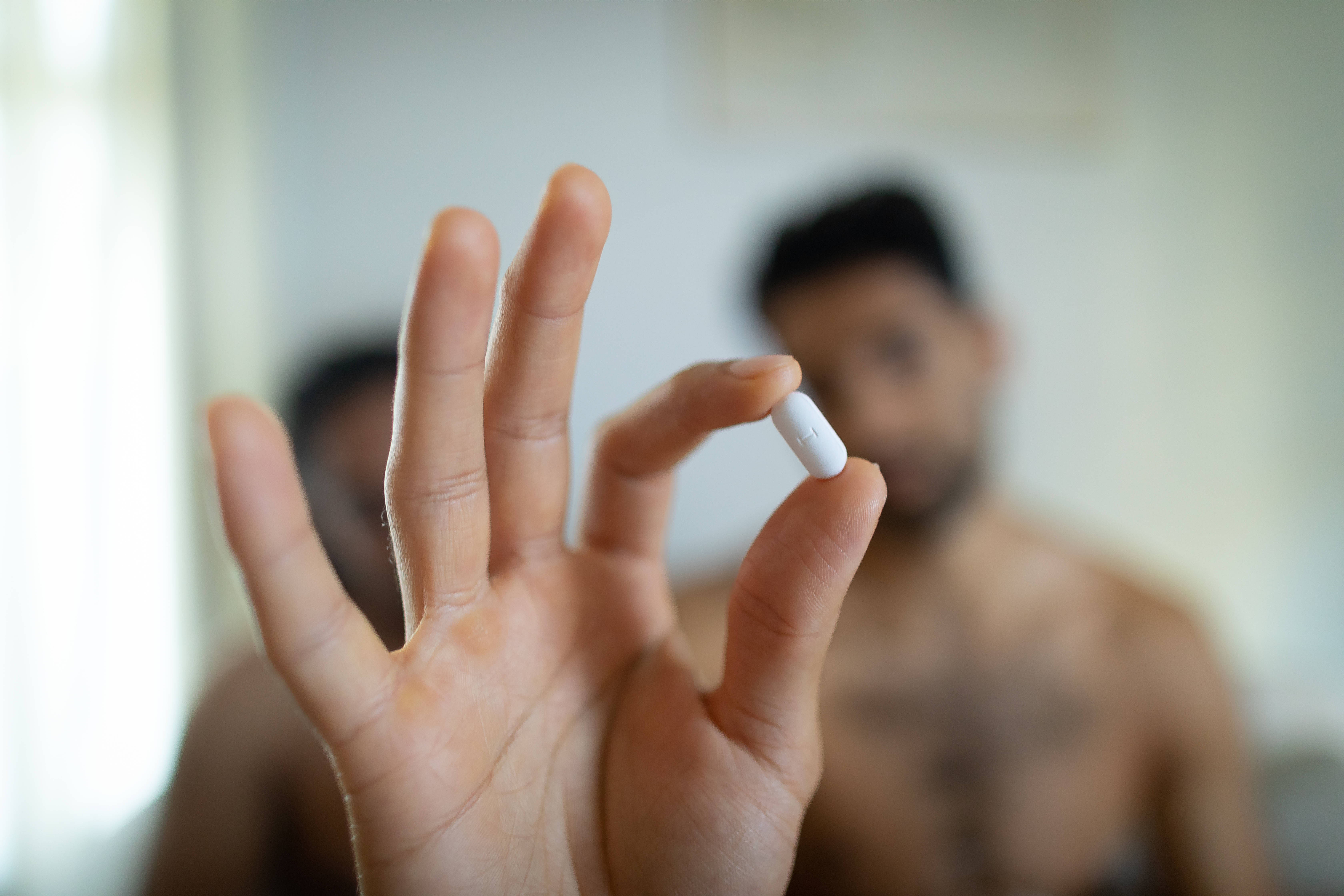 Decorative image - a hand holding a pill with two blurred figures in the background