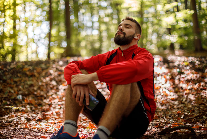 Image of a man sitting in the serene forest on a small hill thinking