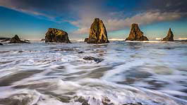 A beach with several rocks coming out of the ocean.