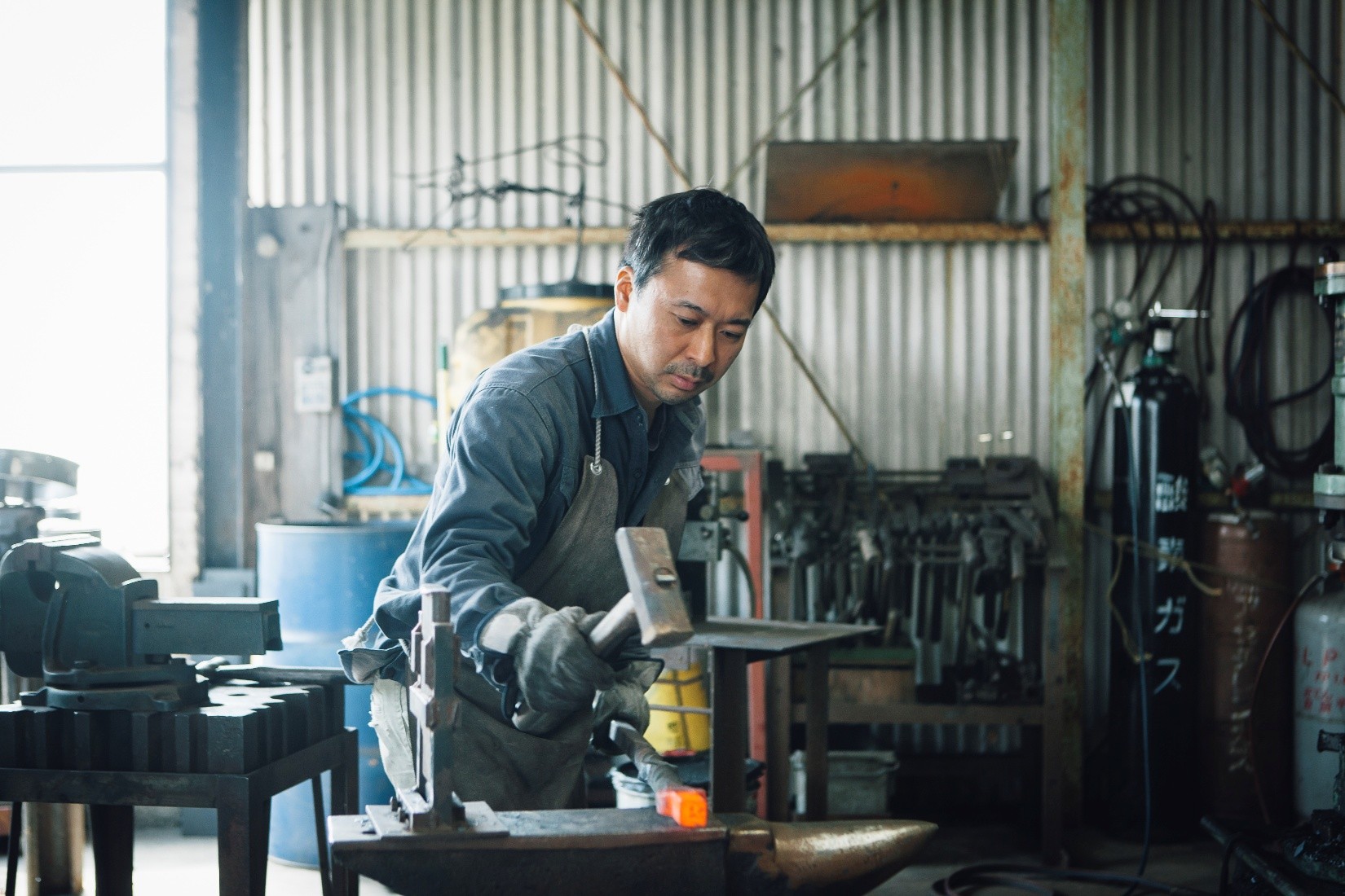 A metalworker shaping a red hot piece of metal.