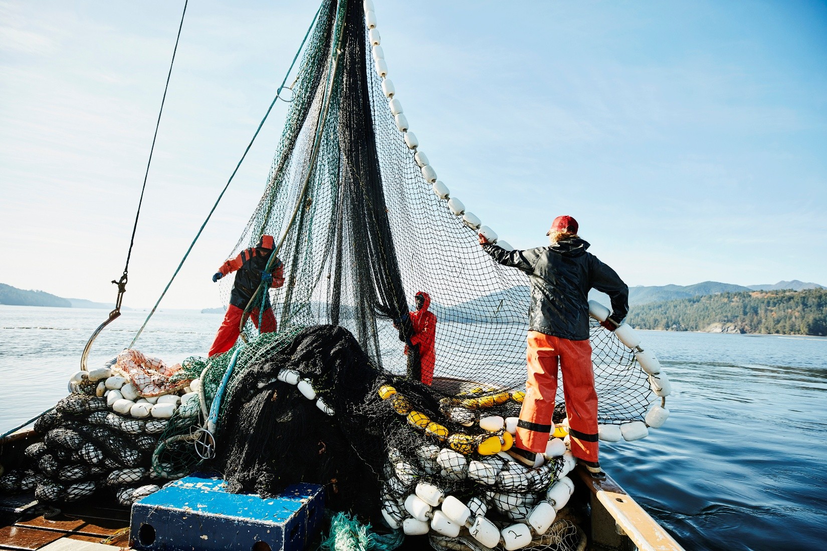 3 workers adjusting a large fishing net on a boat.