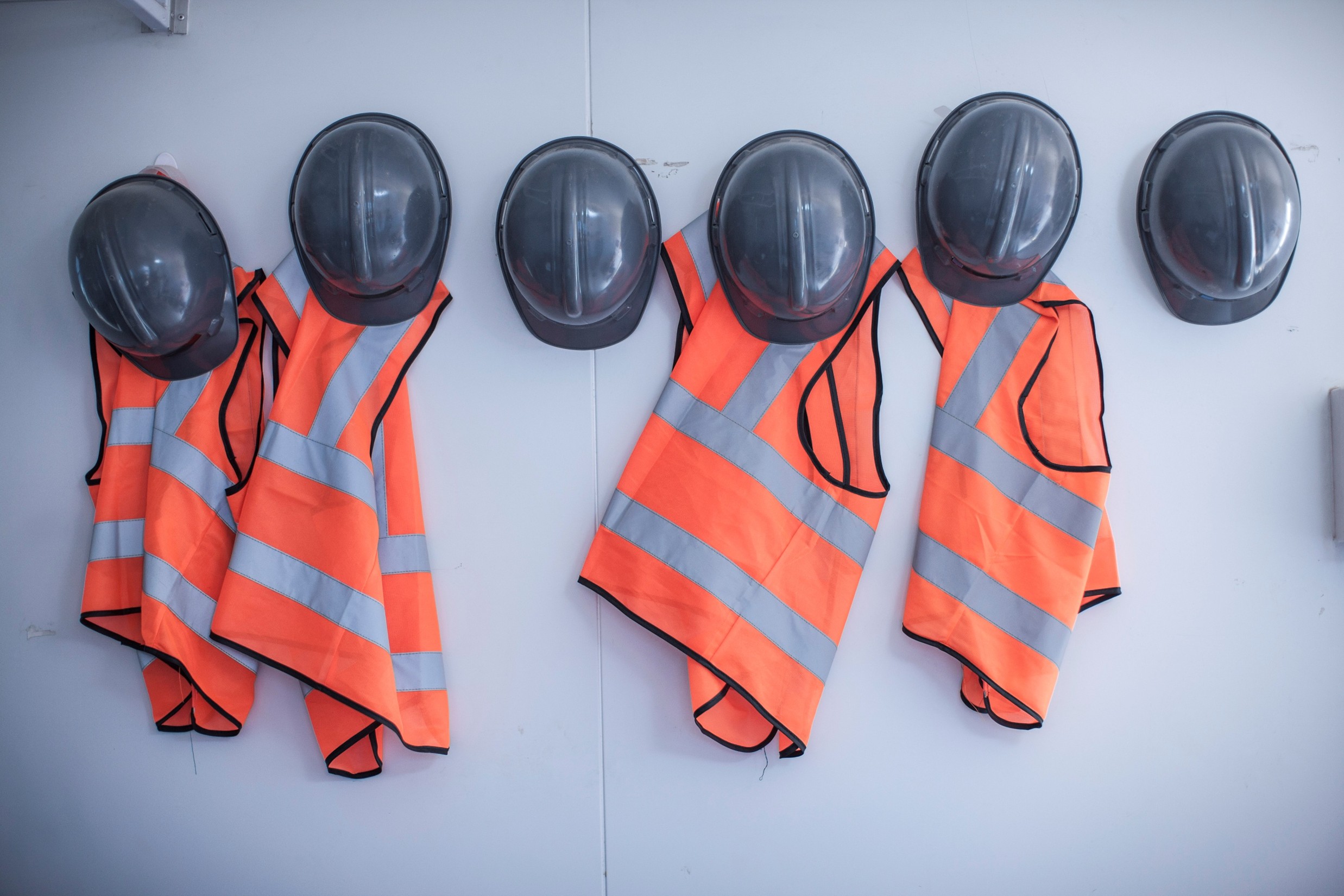 Several black hard hats and orange safety vests hanging on a wall.