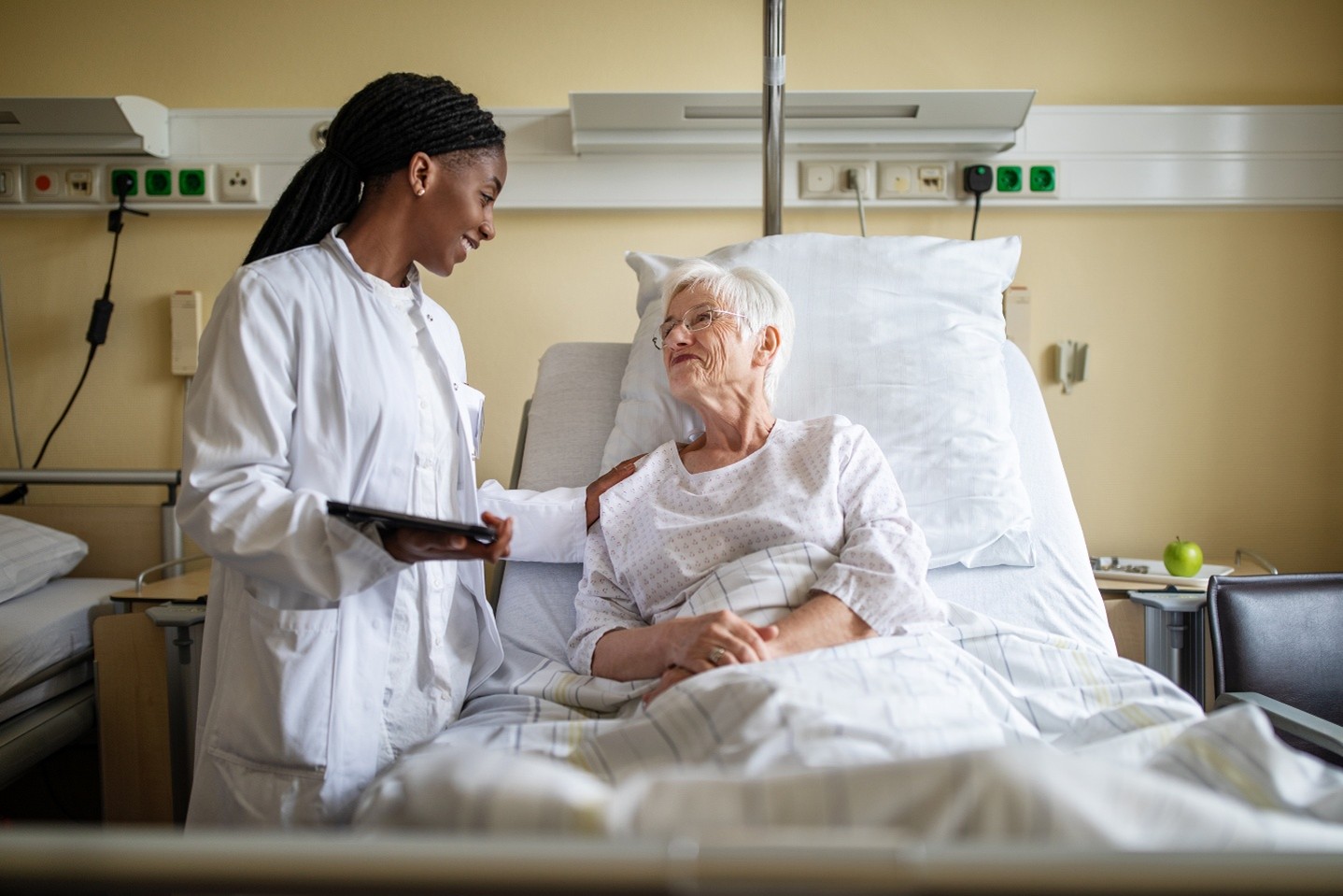 A healthcare profressional puts their hand on the sholder of an older patient in a hospital bed.