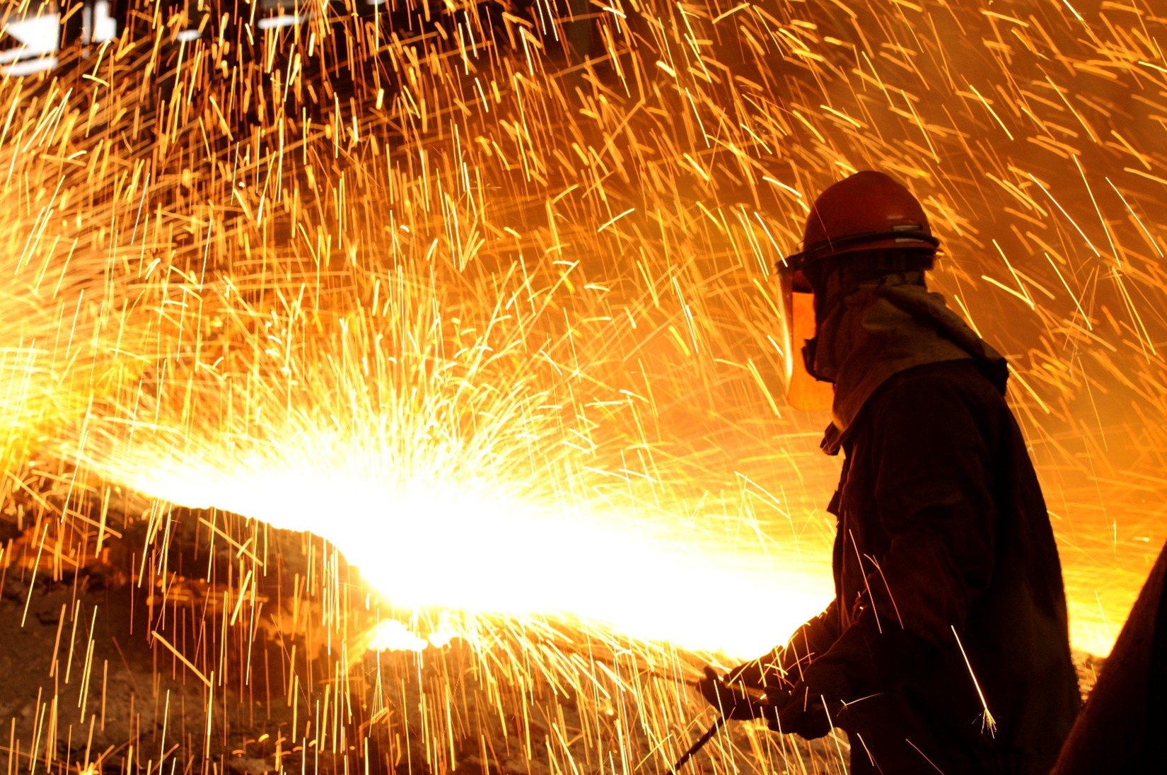 A metal worker surrounded by bright, hot sparks