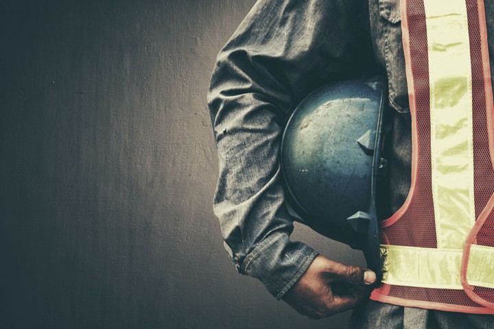 A worker holds a hard hat under their arm.
