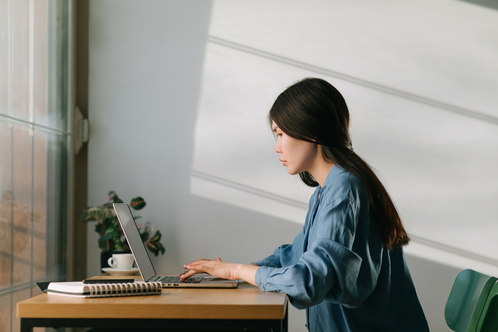 A worker typing on a laptop sitting on a desk in front of them.