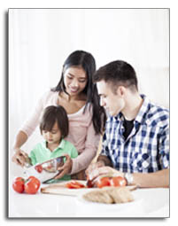  Mother and father helping toddler aged child to put chopped tomatoes into a metal bowl