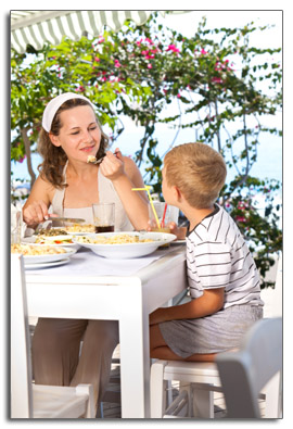  Young woman sitting with a child at an our doors table eating a meal.