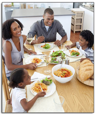  Family of four are sitting at a table together, eating dinner and talking
