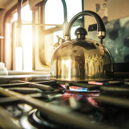 A tea kettle sits on a gas range that's turned on.