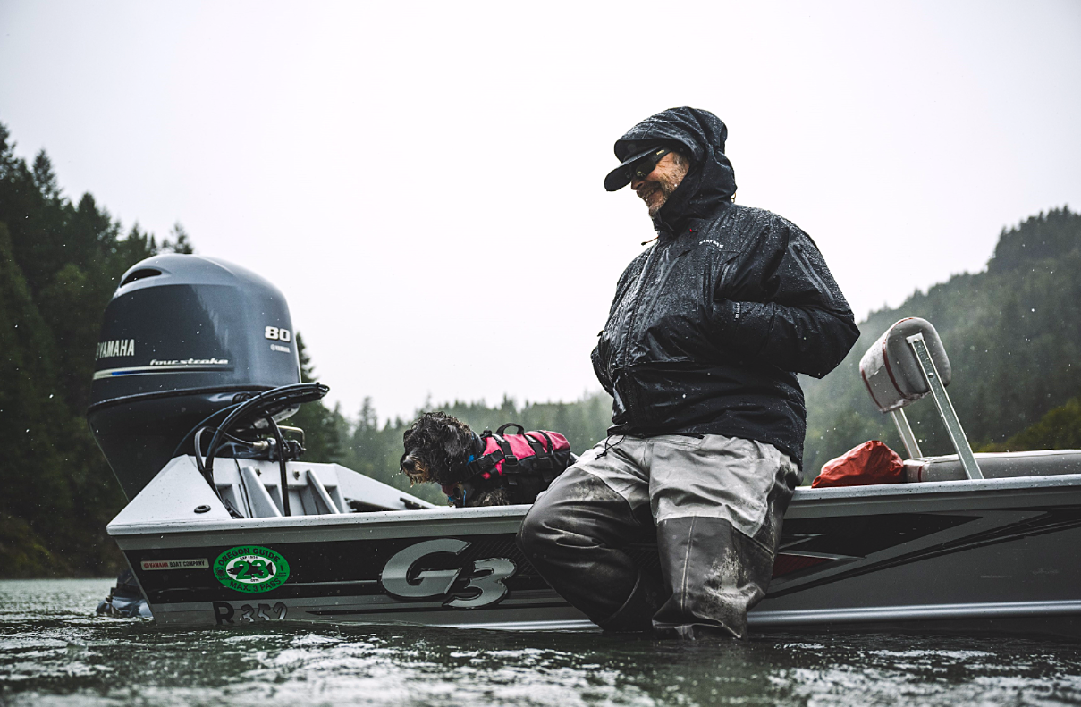 Member Dax Messett sitting on the guwhale of his boat while beached on a river bank