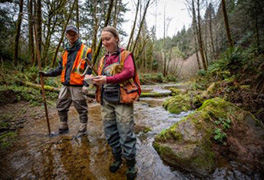two people standing in a creek with survey equipment