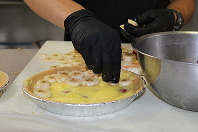 hands place sliced bananas on cream pie.jpg
