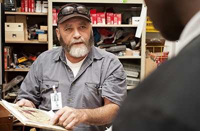 man points at woodworking template, talks to man off camera